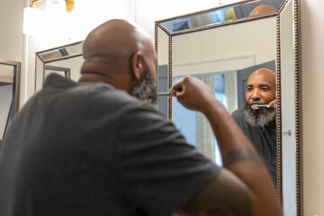 Black man with gray beard brushes teeth in bathroom at home