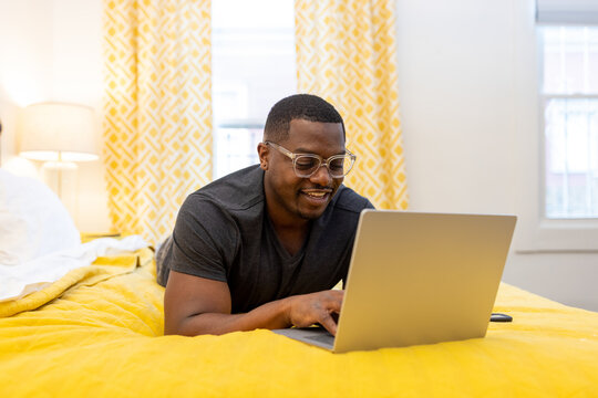 Black man working from home on laptop in bed