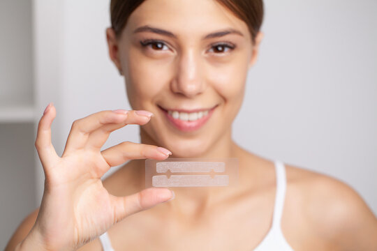 Teeth whitening, beautiful smiling woman holding a whitening strip.