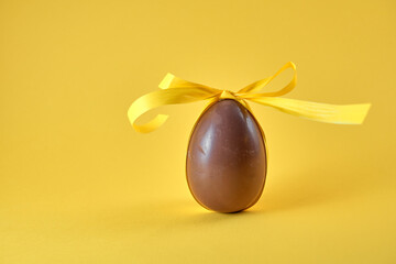 Delicious seasonal chocolate Easter egg with ribbon on a yellow background.
