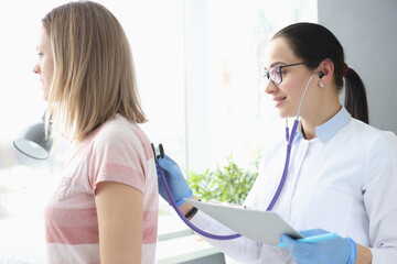 Doctor therapist listens to patient's lungs with stethoscope