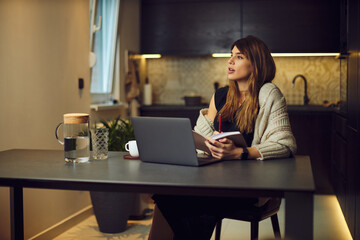 A pregnant brunette sitting at home and reading book. On the table is a laptop.