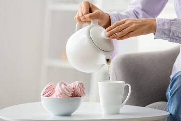 Woman pouring tea from teapot into cup on table in room