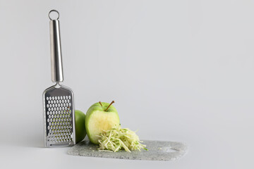 Metal grater and apple on light background