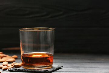 Glass of almond liquor and nuts on dark wooden background, closeup