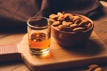 Board with glass of almond liquor and nuts on wooden background