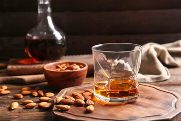 Board with glass of almond liquor and nuts on wooden background