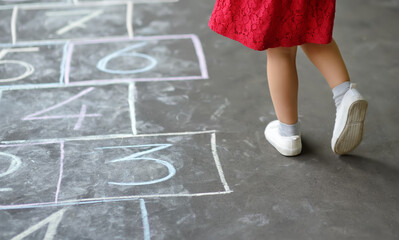 Closeup of little girl's legs and hop scotch drawn on asphalt. Child playing hopscotch game on playground outdoors on a sunny day.