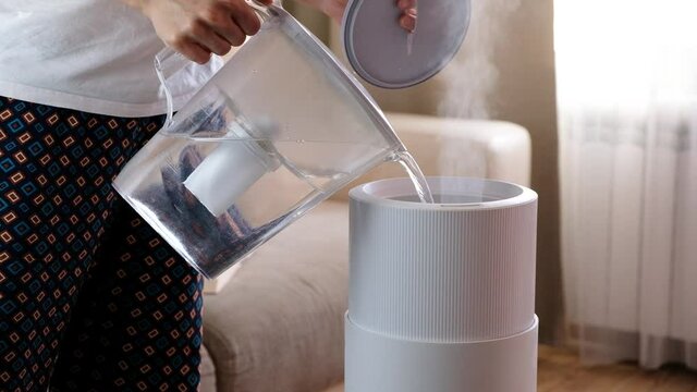 Woman pouring water from the filter to air humidifier, aroma oil diffuser at home. Improving the comfort of living in a house, Improving the well-being. Ultrasonic steam technology.