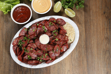 Portion of pepperoni sausage with lemon. Lettuce, green onion, ketchup and mayonnaise