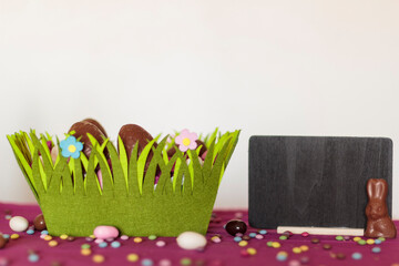 Easter basket with chocolate eggs, chocolate bunny and blackboard with copy space