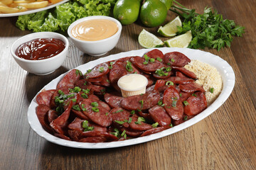 Portion of pepperoni sausage with lemon. Lettuce, green onion, ketchup and mayonnaise