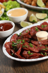 Portion of pepperoni sausage with lemon. Lettuce, green onion, ketchup and mayonnaise