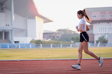 Obraz premium A young Asian woman athlete runner jogging on running track in city stadium in the sunny morning to keep fitness and healthy lifestyle. Young fitness woman runs on stadium track. Sport and recreation
