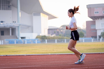 Obraz premium A young Asian woman athlete runner jogging on running track in city stadium in the sunny morning to keep fitness and healthy lifestyle. Young fitness woman runs on stadium track. Sport and recreation