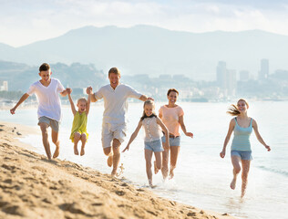 Large active family of six people happily running together on beach on summer day