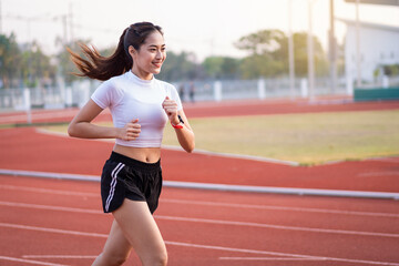 A young Asian woman athlete runner jogging on running track in city stadium in the sunny morning to...