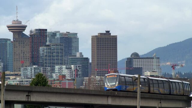 Wide shot of pass train and city skyline of Vancouver in background during cloudy day,Canada.