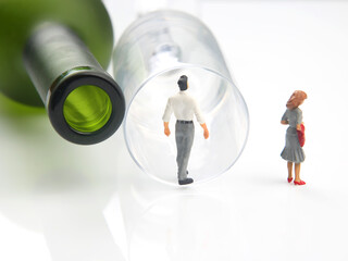 miniature people. man addicted to alcohol on the background of a bottle of wine and a glass and a...