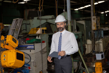 Male mechanical engineer or manager with hardhat uses a tablet to check the operation system in a factory