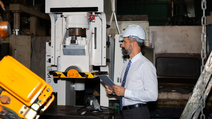 Male mechanical engineer or manager with hardhat uses a tablet to check the operation system in a factory