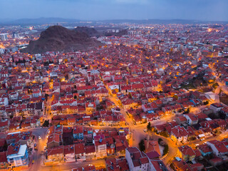 Scenic aerial view of Afyonkarahisar cityscape with lighted streets and similar reddish tiled roofs on residential buildings in winter twilight, Turkey