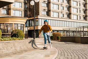 Fototapeta premium Young handsome woman riding on a skateboard. Portrait of sport female model in urban style. Skateboarding at city. Street style outfit. Urban woman ride on skate. Hipster girl on skateboard