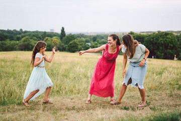 Fun active family weekend in nature. Happy young mother with two daughters is having fun in field...
