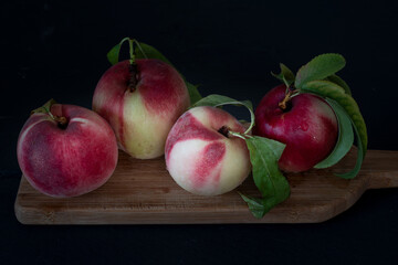 Fresh peaches  with leaves against black background on a wooden board: four whole , viewed form an angle and from close