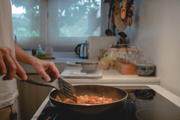 Closeup of man cooking pasta sauce in the kitchen with black pan.