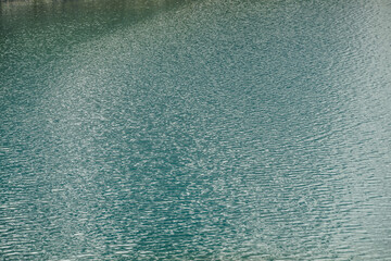 Texture of green blue calm water of lake. Meditative ripples on water surface. Nature minimal background of green blue lake with golden shine. Natural backdrop of lake fragment with clear azure water.