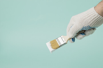 A man wearing gloves holds a brush with dripping white paint on a blue background. © kvladimirv