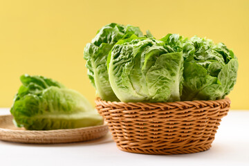 Fresh cos lettuce in a basket on white and yellow background, Organic vegetables