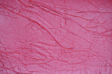 A fragment of genuine leather with wrinkles and folds, artificially dyed in a bright crimson color.