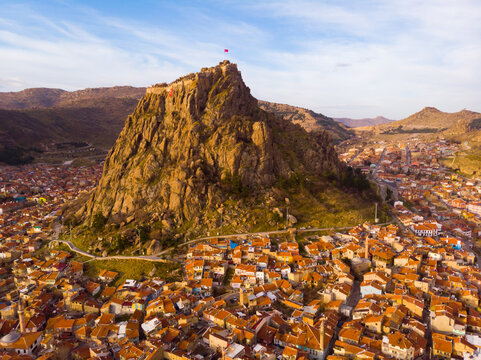View from drone of residential districts of Turkish city of Afyonkarahisar overlooking volcanic rock with ancient ruined castle on top on winter day, Afyon Province