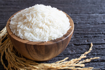 White rice (Thai Jasmine rice) in wooden bowl and paddy rice on dark wooden texture background, Natural food high in protein