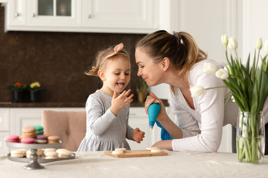 Portrait of little funny girl and her mother baking macarrons and cookies in the kitchen. Happy family and mother's day concept