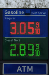 Fototapeta premium Fuel price display board showing regular gasoline at $3.05⁹ and diesel No. 2 at $2.89⁹ per gallon, with self-serve and ATM signage at a retail gas station during daytime