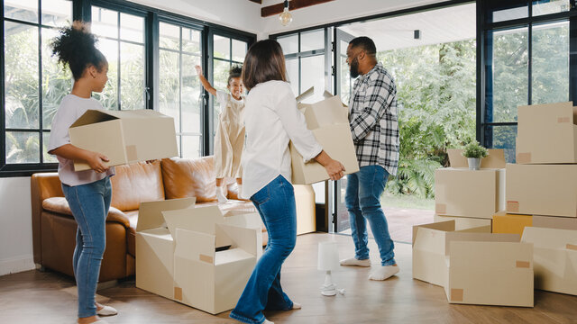 Happy African American young family bought new house. Mom, Dad, and child happy hold cardboard boxes for move object and having fun laugh into modern home. New real estate dwelling, loan and mortgage.