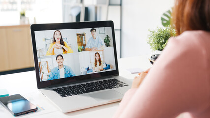 Young Asia businesswoman using laptop talk to colleague about plan in video call meeting while work from home at living room. Self-isolation, social distancing, quarantine for corona virus prevention.