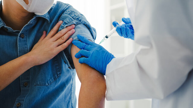 Young Asia lady doctor giving Covid-19 or flu antivirus vaccine shot to senior male patient wear face mask protection from virus disease at health clinic or hospital office. Vaccination concept.