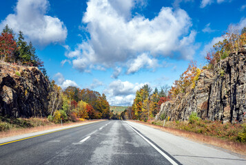 Fototapeta premium Landscape with a highway and picturesque autumn maple trees on roadside cliffs in Vermont