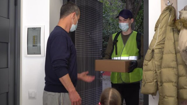 Help and support during COVID-19: Volunteer, Donate. A man courier in protective mask and medical gloves. Father and child pick up the parcel. Lockdown and social distancing during coronavirus
