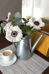 Delicate anemones flowers in metal pot vase with cup of coffee on the table