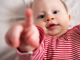 Portrait of a baby girl, 8 months old, looking at the camera, pointing at the camera, top view, close-up. A mischievous, beautiful girl with fair skin and hair, with big blue eyes