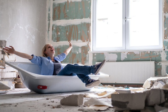 Renovation Home. Excited Woman Sits In Bathtub In The Middle Of The Room Raising Arms. Empty Walls, Repairs House With Their Own Hands.