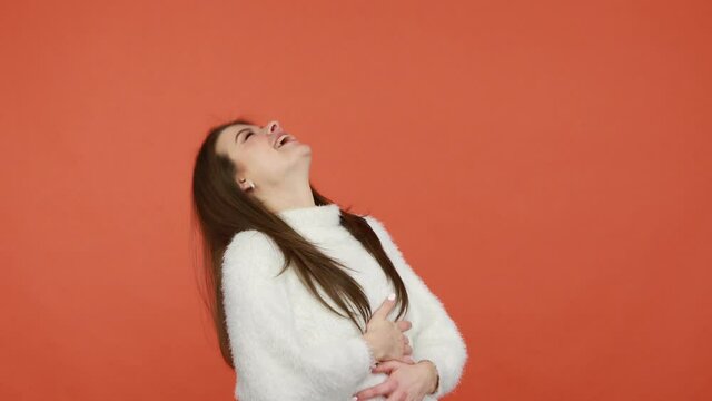 Excited shocked brunette woman in white fluffy sweater pointing finger and laughing out loud, surprised with your success, ridiculing and mocking you. Indoor studio shot isolated on orange background