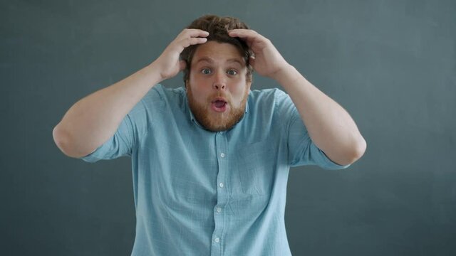 Portrait of surprised guy raising arms and opening mouth expressing excitement and amazement standing alone against gray background and looking at camera