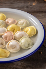 Traditional Russian dumplings made from multi-colored dough in broth. Dumplings on a wooden board in an enamel plate. Cooking concept.