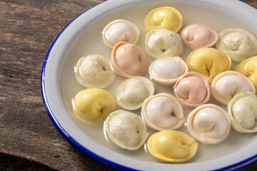 Traditional Russian dumplings made from multi-colored dough in broth. Dumplings on a wooden board in an enamel plate. Cooking concept.